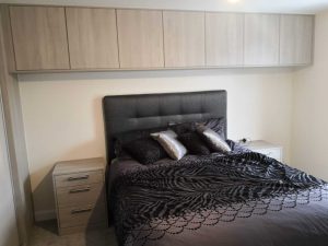 bed with row of cupboards above it and beside tables